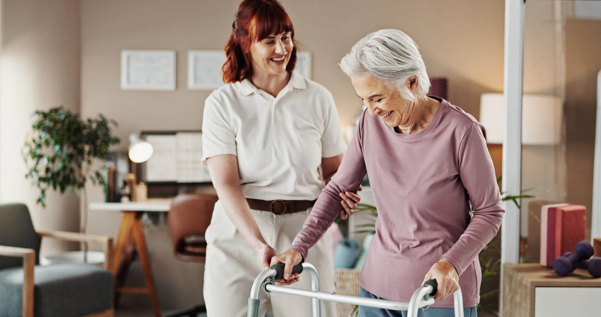 Pflegekraft begleitet eine Seniorin mit Rollator im Wohnbereich