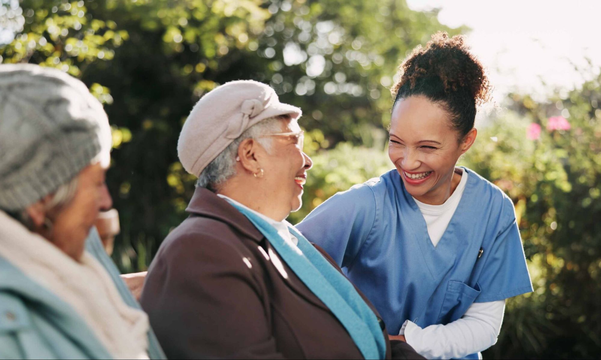 Pflegekraft spricht mit zwei Seniorinnen im Garten